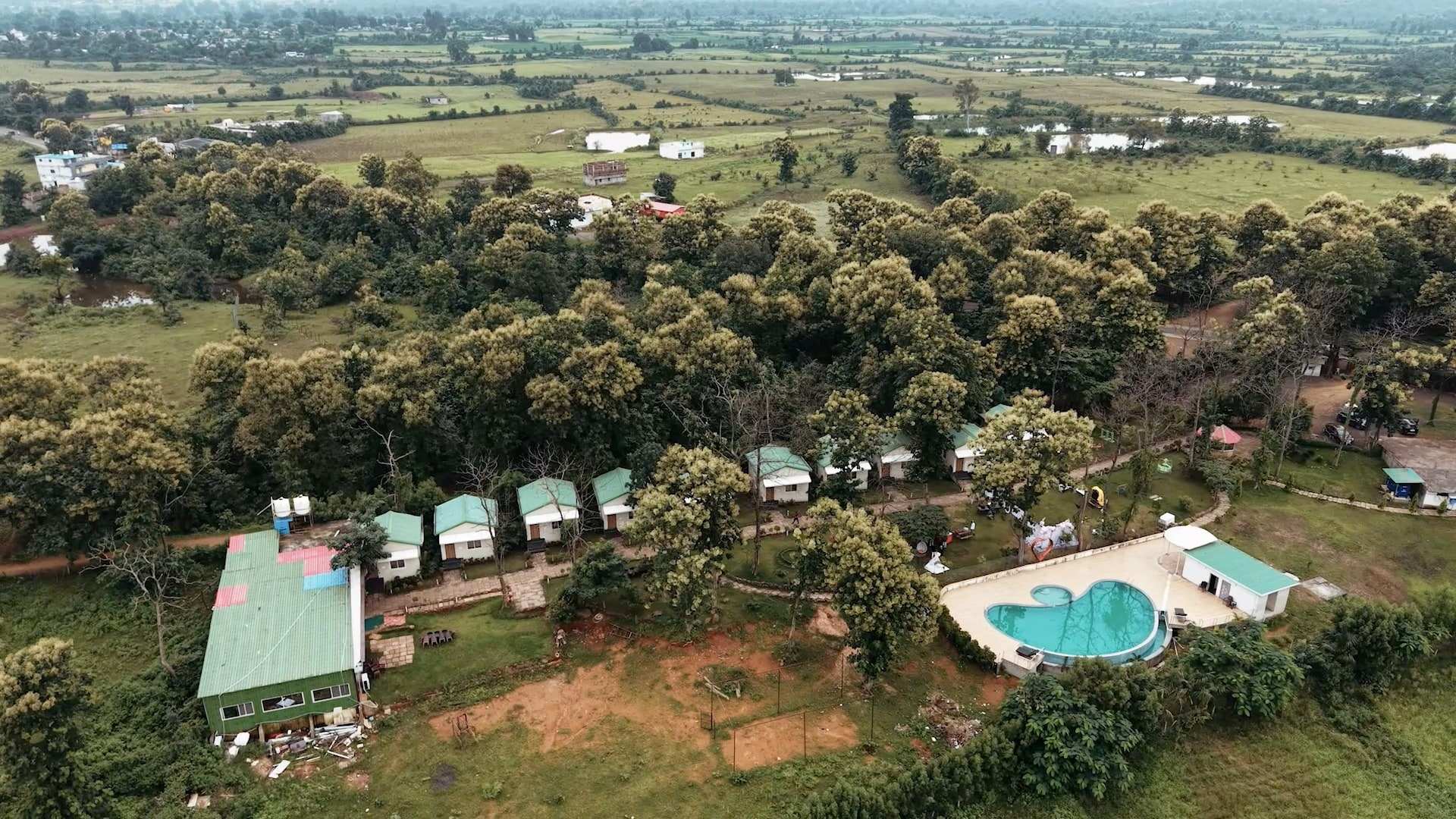 Aerial view of the resort: a row of cottages, the dining hall and the swimming pool among trees and fields