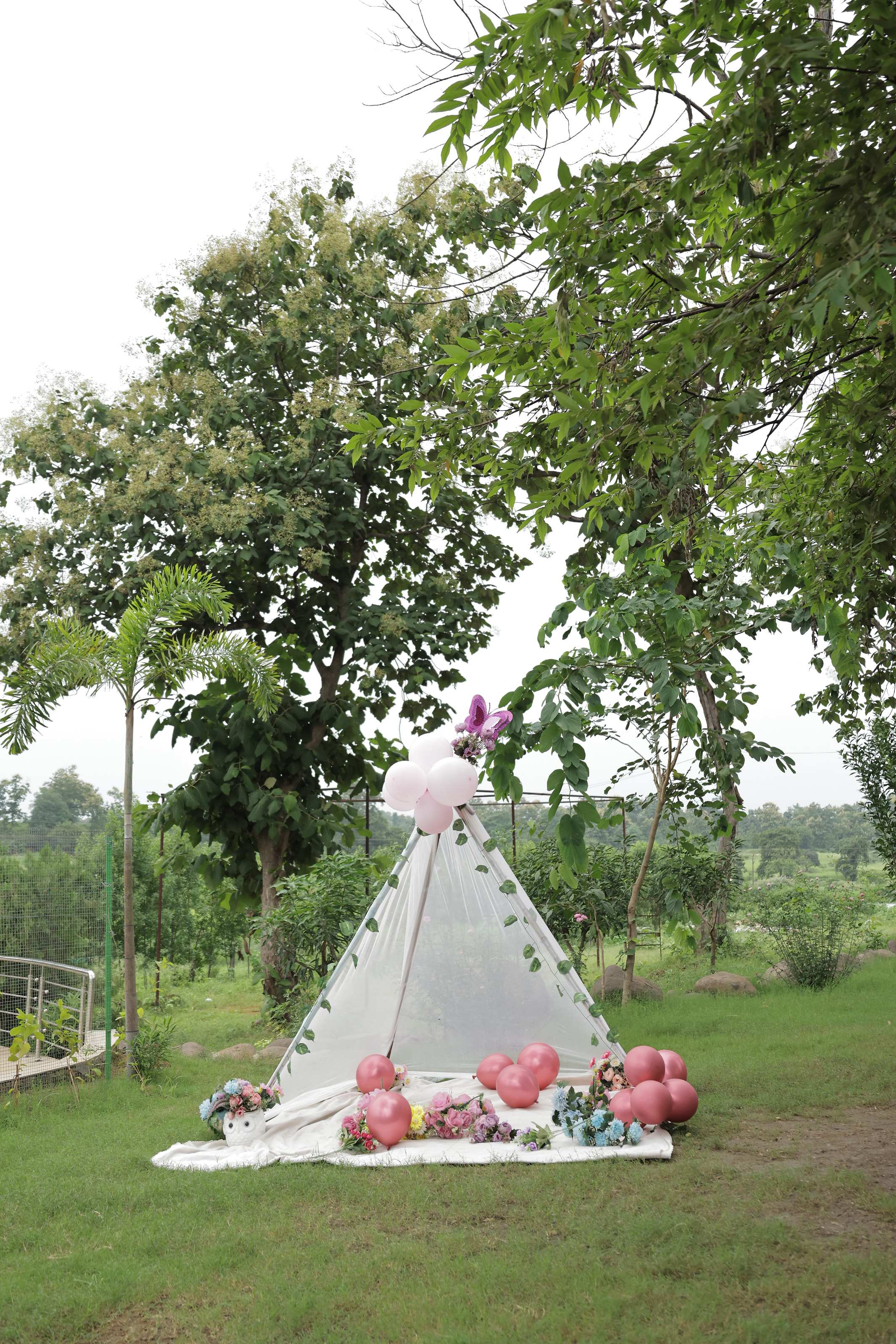 White teepee with balloons and flowers set up on the lawn under tall trees