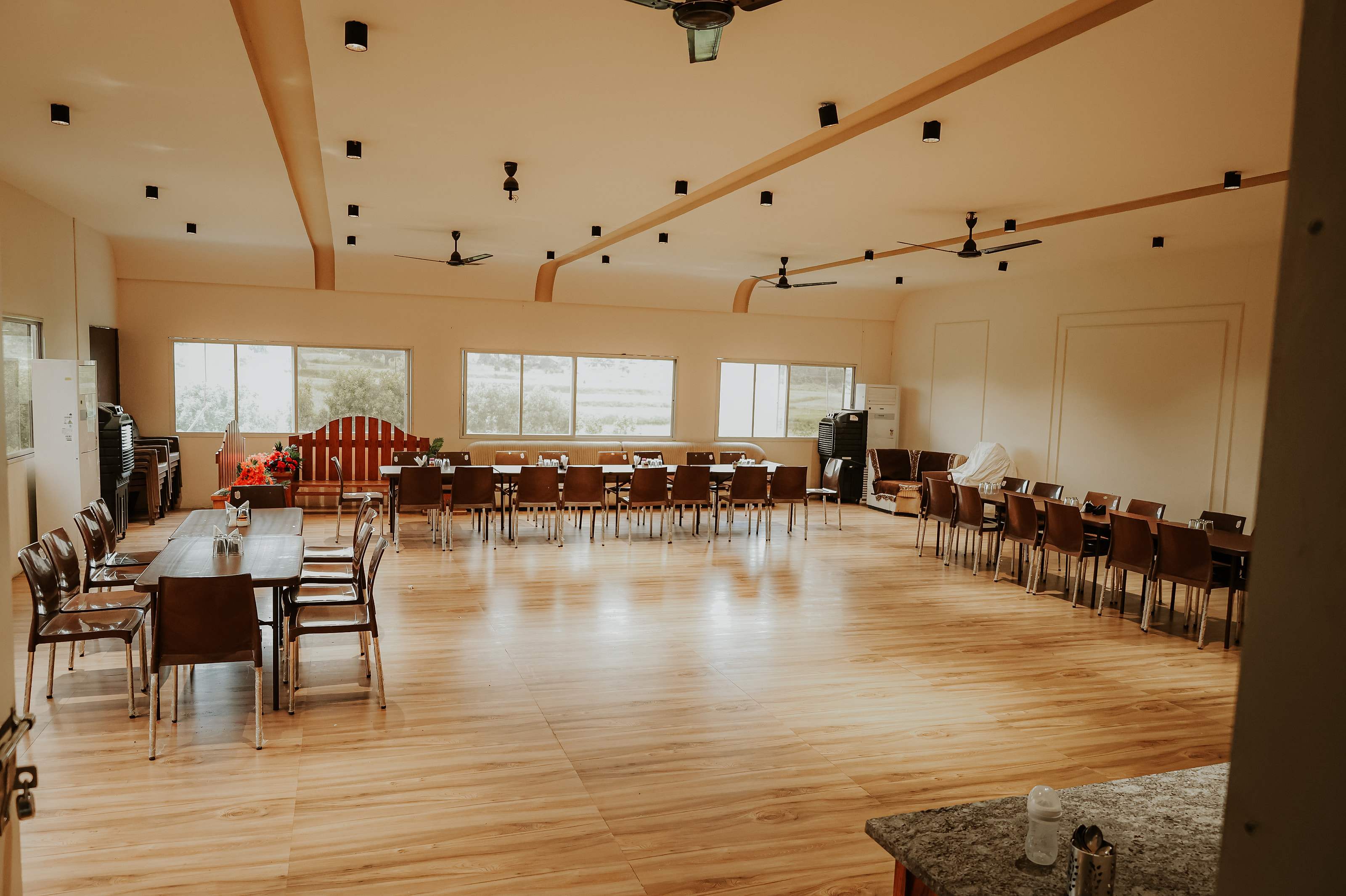 Bright dining hall with long tables, wooden floor and windows onto the garden