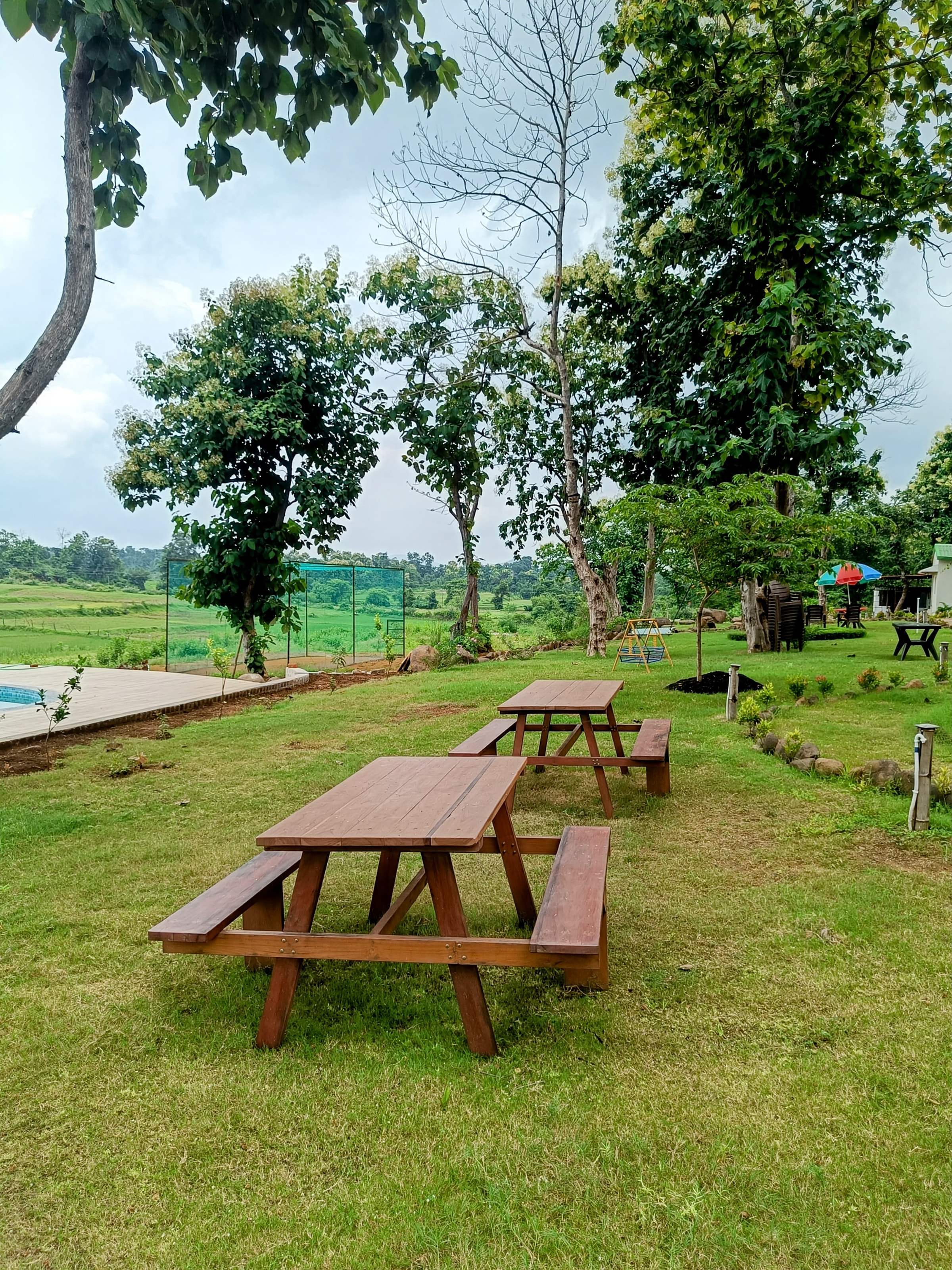 Wooden picnic tables on the lawn under trees, with fields beyond