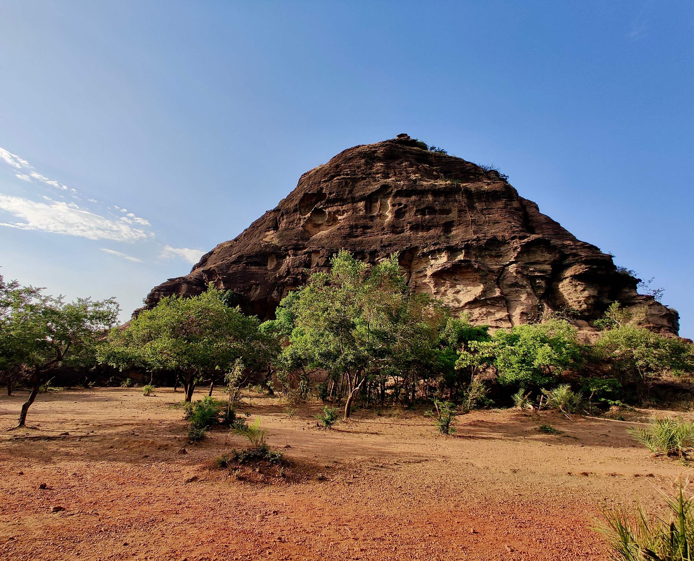 A great dome of layered sandstone rising above trees near Dhoopgarh