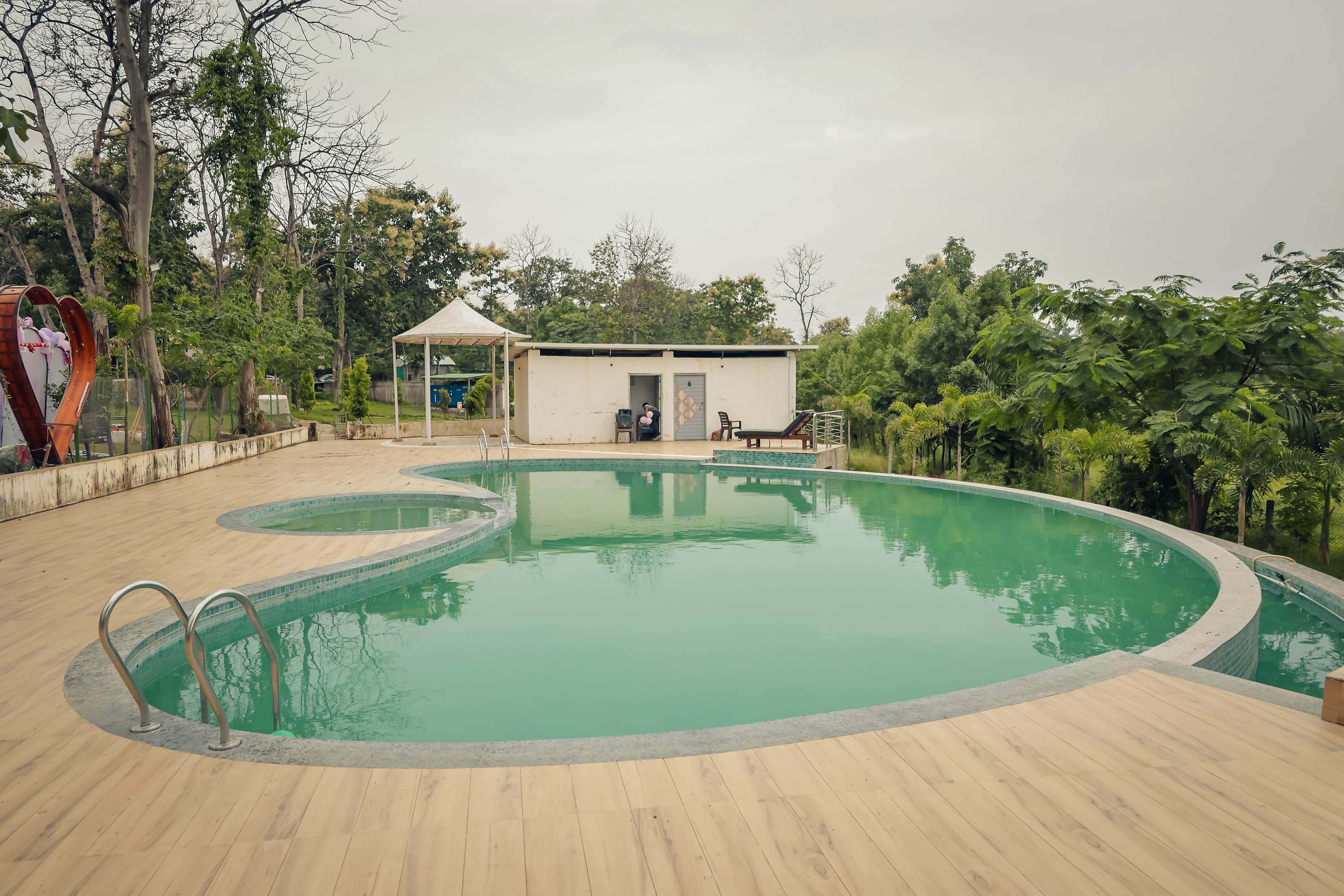 Swimming pool with wooden deck and changing rooms, surrounded by trees