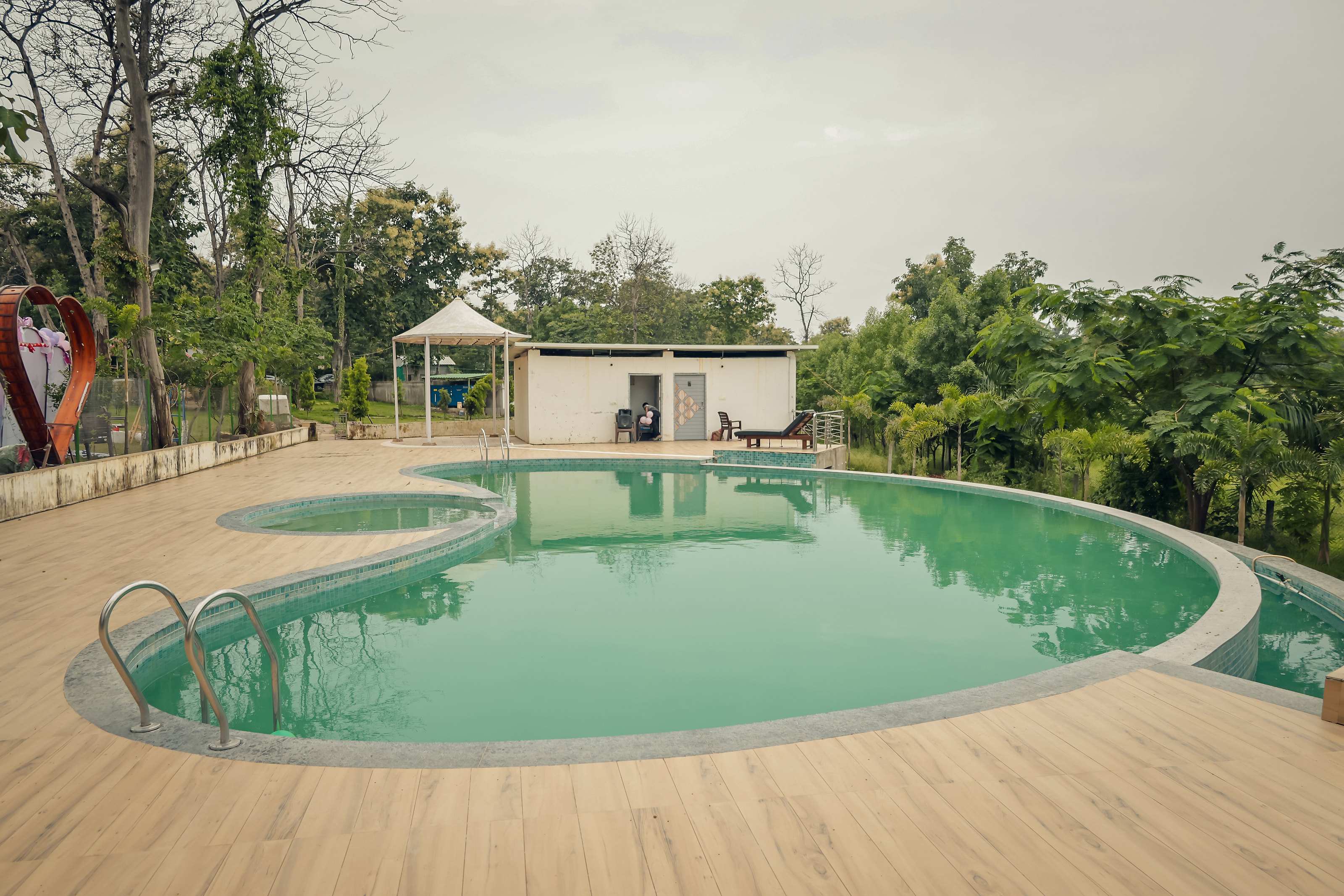 Swimming pool with wooden deck and changing rooms, surrounded by trees