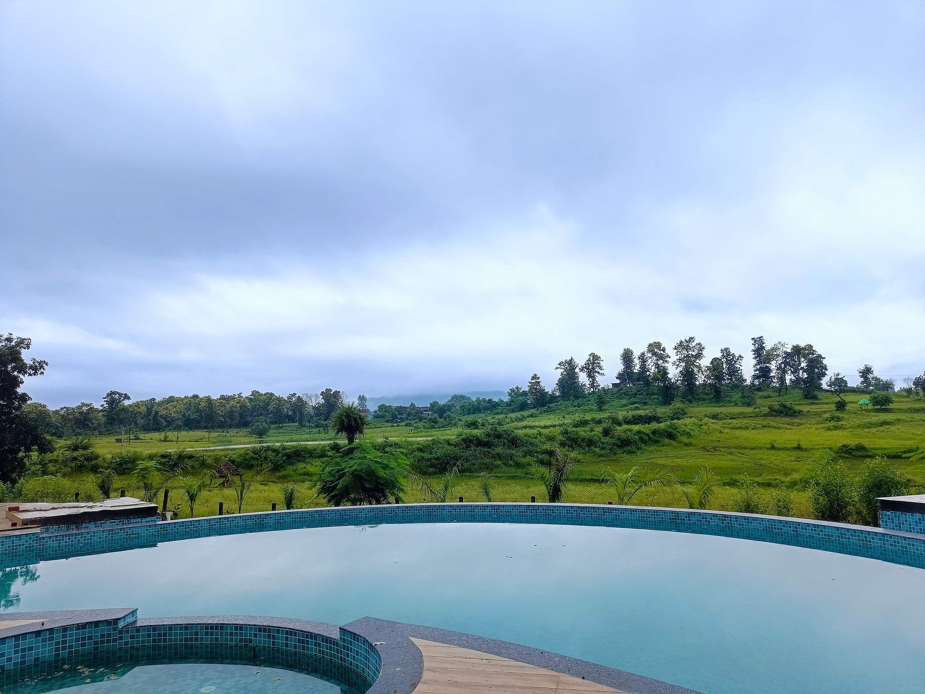 View across the pool edge to open green fields and distant hills under monsoon cloud
