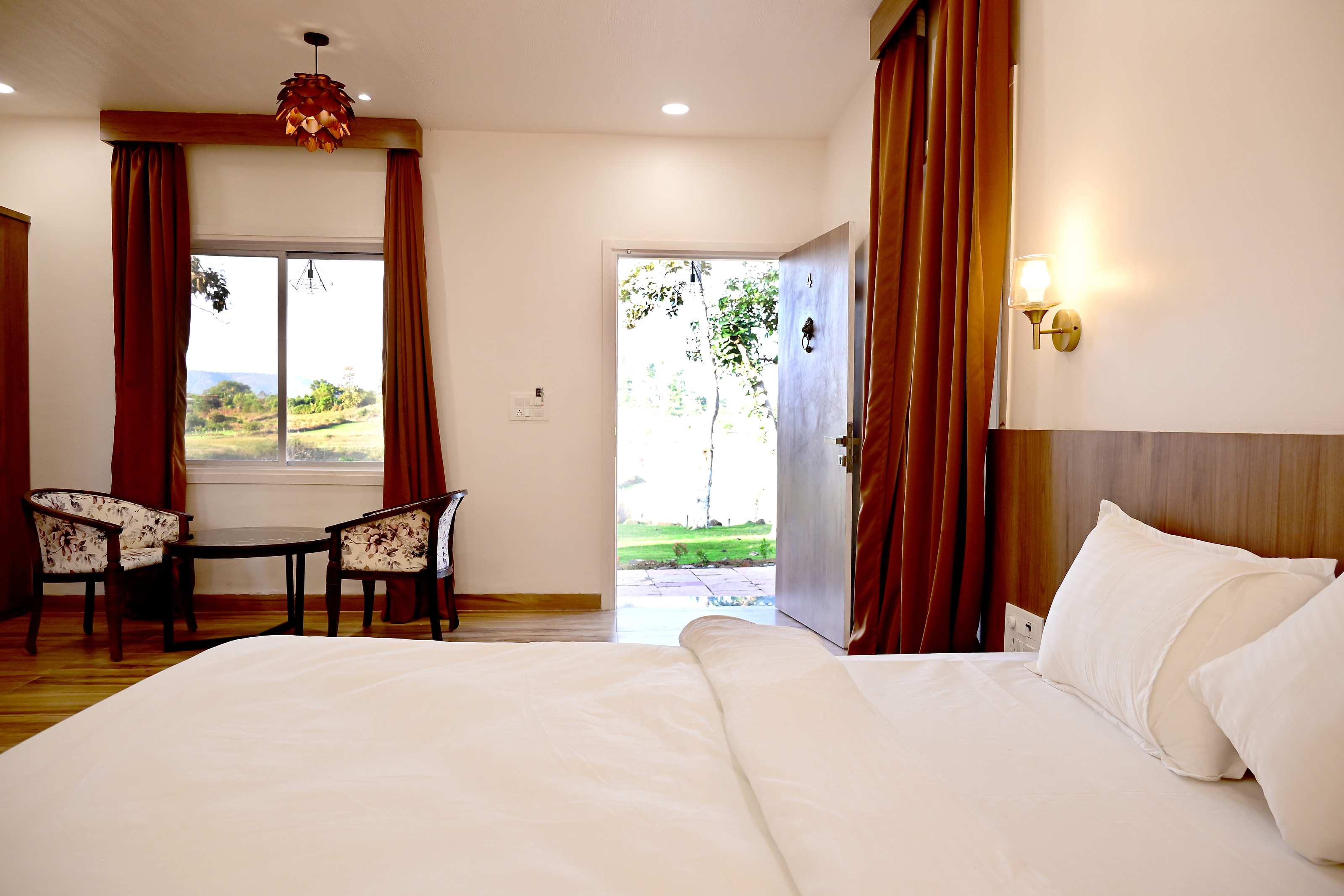Cottage interior: white bed in the foreground, two chairs by the window and the door open to the lawn